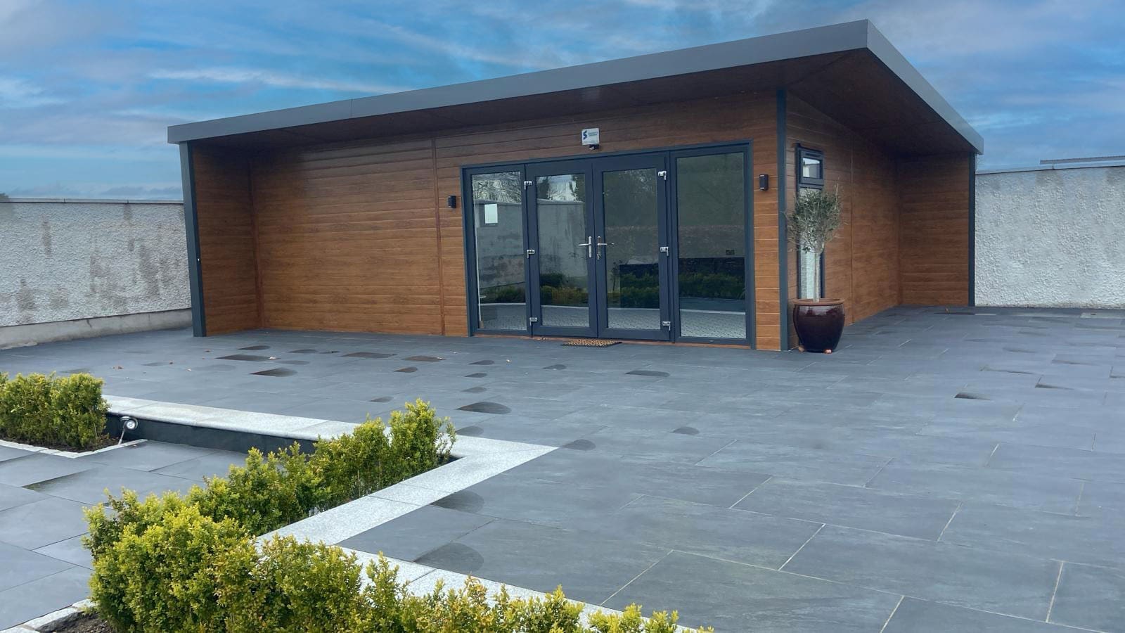 8 m × 5 m insulated steel garden room clad in golden oak composite panels with floor-to-ceiling glazing